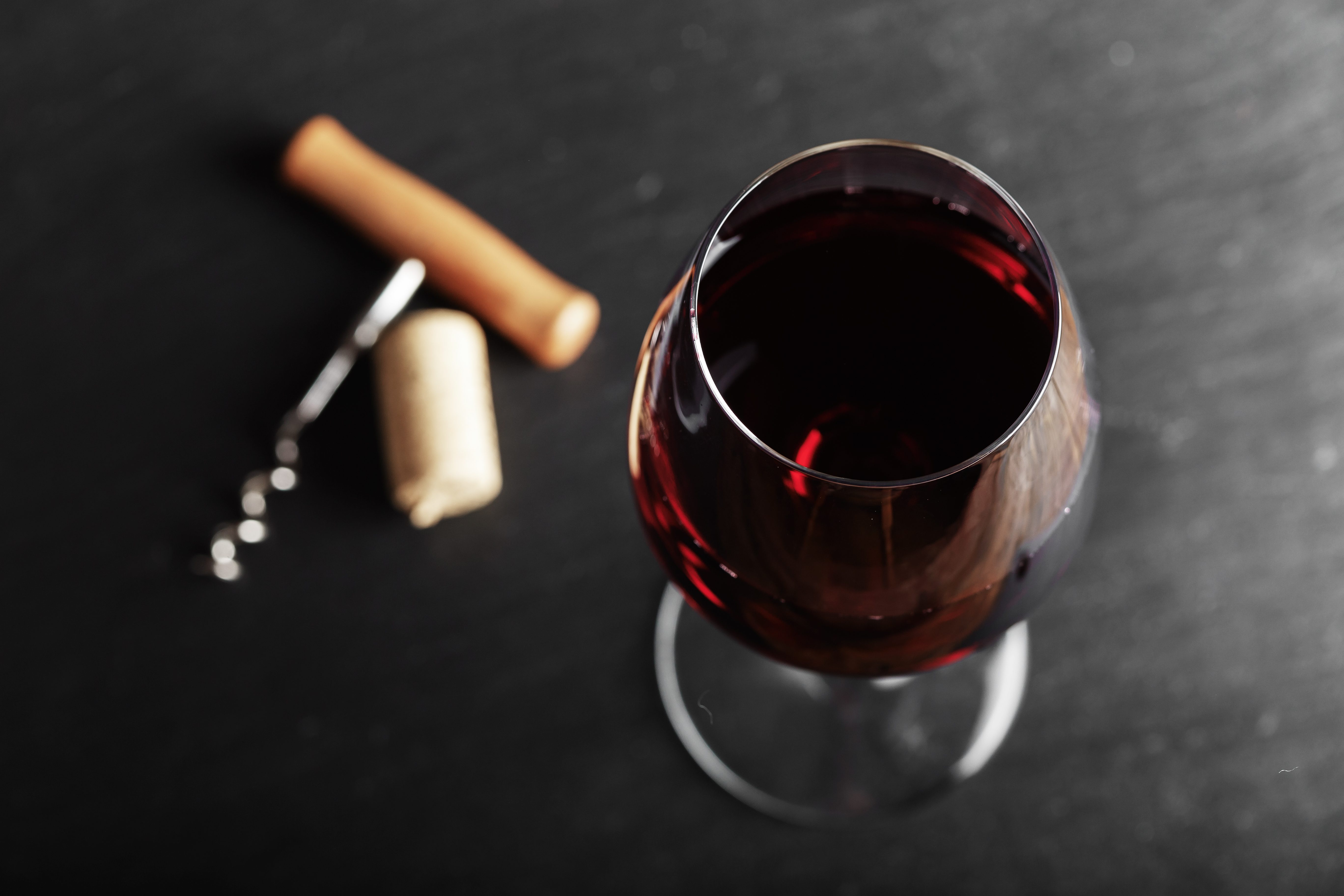 wine glass of red wine with a corkscrew. On a black wooden background. 